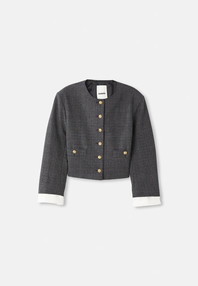 Geknipte grijze geruite blazer met gouden knopen, witte manchetten, ronde halslijn en twee voorzakken. Gevoerde binnenkant.