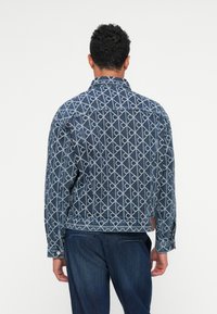 Jeans jakna s plavim geometrijskim uzorkom, s oštrim ovratnikom, zatvaranjem na dugmad i dugim rukavima. Tekstura uključuje detalj na le�đima.