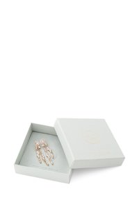 Pendientes de oro rosa con cristales transparentes, exhibidos en una caja gris suave con un acabado texturizado y logo dorado. La caja está abierta, mostrando los pendientes de manera ordenada.