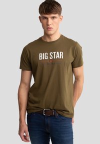 Aliejinės žalios medvilnės marškinėliai su apvalia kaklo iškirpte, ant kurių yra rašytas "BIG STAR" baltomis ir raudonomis spalvomis. Lygi tekstūra, prigludęs dizainas.