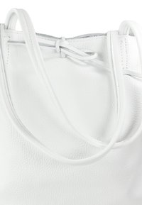 Sac fourre-tout en cuir blanc avec surface texturée, présentant des straps étroits et un détail de fermeture noué. Design minimaliste, finition douce.