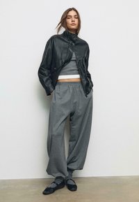 Crna kožna jakna s visokim ovratnikom, sivi skraćeni top, labave sivo prugaste hlače i crne balerinke sa sivim čarapkama. Glatka textura kroz cijeli look.