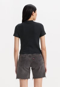T-shirt en coton noir à manches courtes, porté avec un short en denim gris avec un ourlet brut et des coutures visibles sur les poches arrière.