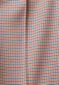 Houndstooth-mönstrad tyg i vitt, marinblått och orange. Mjukt textur med distinkta geometriska former som skapar ett klassiskt, strukturerat utseende.