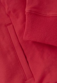 Czerwona bluza z gładkiego materiału, z prążkowanymi mankietami oraz boczną kieszenią z subtelnym detalem szwu.