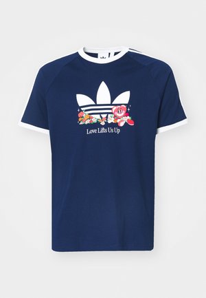 T-shirt bleu marine avec col blanc et bord de manche blanc, avec un grand logo blanc, des fleurs colorées, un personnage en forme de cœur, et le texte "Love Lifts Us Up".