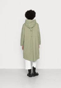 Długi, oliwkowozielony płaszcz z kapturem. Posiada talię ściśniętą, duże kieszenie i prosty krój. Nosi się go z białymi spodniami 3/4 i czarnymi butami.