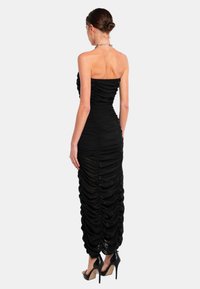 Zwart strapless maxi-jurk met geplooide stofdetails, een aansluitende silhoutte en een slank ontwerp dat tot op de grond reikt.