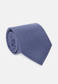 Námořnická modrá kravata so geometrickým bielym vzorom, vyrobená z textúrovaného materiálu, stočená do valcového tvaru. Viditeľný trojuholníkový koniec.