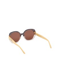 Gafas de sol con un frontal redondeado, oscuro y translúcido, y lentes marrones; las varillas amarillas presentan un diseño geométrico.