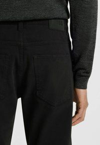 Czarne spodnie slim fit z teksturowanego, miękkiego materiału. Posiadają dwie tylne kieszenie oraz prostokątną metkę z logo na pasie.