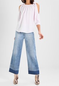 Vaaleanpunaisessa raidallisessa puserossa on kylmät olkapäät, ja se on yhdistetty vaaleansinisiin leveälahkeisiin farkkuihin, joissa on tummempi helma. Mallilla on päällään metallinhohtoiset roosa-kultaiset kengät.