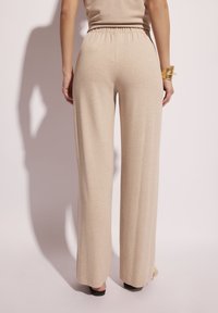 Jasnobeżowe, wysokie spodnie z szerokimi nogawkami, z elastycznym paskiem i miękką teksturą, charakteryzujące się luźnym krojem i minimalnymi detalami szwów.