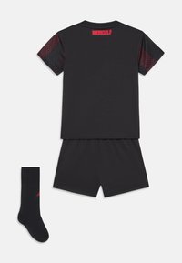 Tenue de sport noire comprenant un haut à manches courtes avec des accents rouges et un short assorti, accompagné de chaussettes noires.