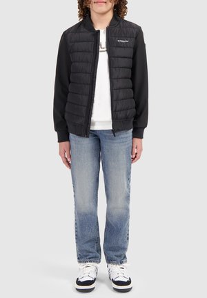 Zwart gewatteerd bomberjack met een rits, gebreide boorden en zachte stof; gecombineerd met lichtblauwe jeans en zwarte sneakers.