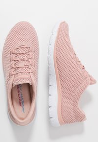 Baskets en maille rose clair avec une surface texturée, dotées de semelles en caoutchouc blanc et de lacets, brandées "Skechers Memory Foam" à l'intérieur.