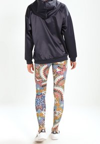 Sportig jacka i marinblå, ihopparad med färgglada mönstrade tights med blommönster och geometriska designer, båda i sällskap av vita sneakers.