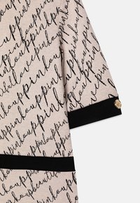 Lyserød genser med et sort håndskrevet mønster med "love" og "pink", accentueret af en kraftig sort manchet og en detalje med en guldknap.