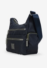 Bolso de hombro de nylon marino con dos bolsillos frontales con cremallera, correa ajustable y acentos de hardware plateado. Presenta un parche de logo texturizado.