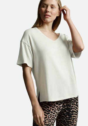 Helles beige V-Ausschnitt-T-Shirt mit kurzen Ärmeln, lockerer Passform und seitlichen Schlitzen. Kombiniert mit Leggings in Schwarz und beigefarbenem Leopardenmuster. Weicher Stoff.