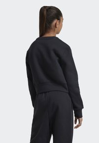 Sudadera corta negra hecha de tejido suave, con mangas largas, escote redondeado y dobladillo acanalado. Diseño minimalista.