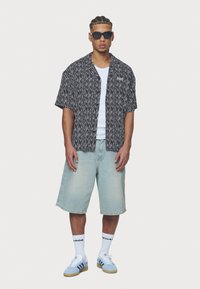 Camisa de manga curta com padrão em preto e branco, top branco, calções de ganga azul-claro, meias brancas, ténis azuis e óculos de sol pretos.