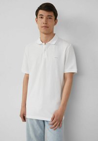 Weißes Poloshirt mit einem Knopfleistenkragen, kurzen Ärmeln und einem dezenten Logo. Getragen mit hellblauen Jeans aus Denim. Einfaches und sauberes Design.
