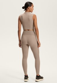 Top sportivo beige a maniche corte e leggings realizzati in un tessuto morbido e elasticizzato. I leggings presentano una vita a costine e un design senza cuciture.