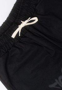 Pantaloni corti neri con una vita arricciata e un laccio bianco. Il tessuto presenta una lieve texture con un delicato motivo visibile.