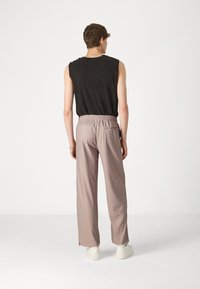 Top noir sans manches associé à un pantalon large de couleur violet clair. Le pantalon a une taille élastique et une poche arrière. Baskets blanches.