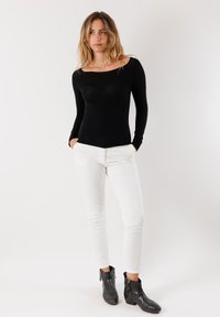 Top nero a maniche lunghe con scollatura a barca, abbinato a pantaloni bianchi attillati e stivaletti neri con zip. Design semplice e aderente.