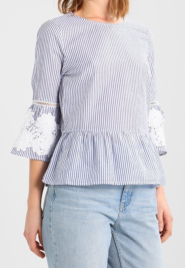 Top in cotone a righe con peplum, maniche a campana 3/4, caratterizzato da dettagli in pizzo ai margini delle maniche. La combinazione di colori include righe blu e bianche.
