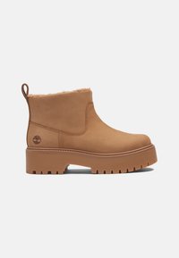 Bottes en cuir tan à chevilles avec doublure en shearling, une semelle en caoutchouc épaisse et une languette de traction. Comprend un logo embossé sur le côté.