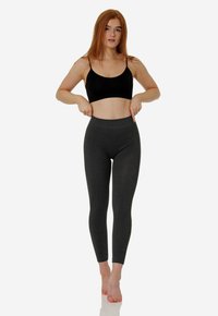 Reggiseno sportivo nero e leggings grigio scuro a vita alta realizzati in tessuto elasticizzato; texture liscia, design aderente, lunghezza fino alla caviglia.
