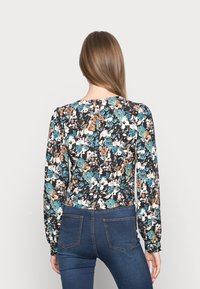 Blusa de manga longa com padrão floral em preto, verde-água e laranja, com decote redondo e punhos elásticos, combinada com jeans azuis.