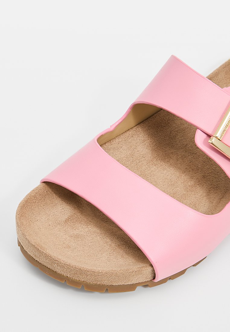 Sandale en plastique rose avec deux larges bandes, une semelle intérieure beige douce et une semelle extérieure en caoutchouc texturé. Accentuée par des détails en métal doré.