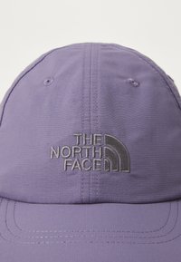 Purple fabric cap with stitched details, featuring a dark gray embroidered "The North Face" logo on the front. Smooth texture, curved brim.