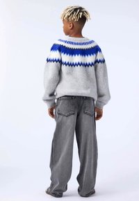 Gray sweater with blue and white zigzag pattern on shoulders, paired with loose-fitting gray jeans. Textured fabric with ribbed cuffs.