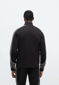 Čierna mikina s vysokým golierom, sivými bočnými panelmi a bielymi lemami pozdĺž ramien. Hladká textúra látky.