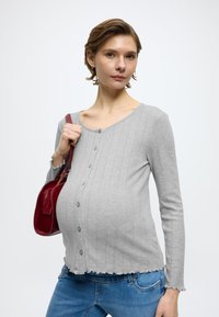 Svetlosivý rebrovaný top s dlhým rukávom a výstrihom do V, s gombíkmi vpredu, zvlneným lemom, doplnený červenou kabelkou na rameno.