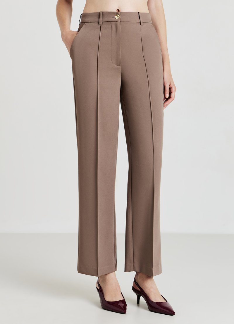 Pantalon marron ajusté à taille haute avec deux poches avant, un pli cousu et une fermeture à bouton doré. Tissu lisse, coupe droite.