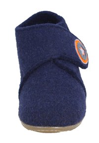 Chausson en feutre marine avec un bout arrondi, une bande auto-agrippante et un patch circulaire gris et orange sur le côté. Semelle plate et texturée.