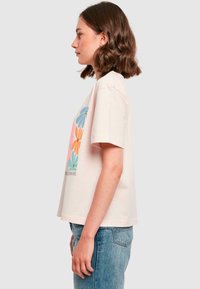 Light pink short-sleeve t-shirt featuring a floral design in blue, orange, pink, and green. Casual fit with a straight hem and soft texture.
