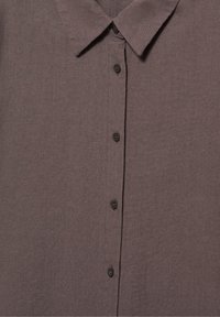 Chemise marron à boutons avec un col pointu et cinq boutons visibles le long de la patte de boutonnage avant.