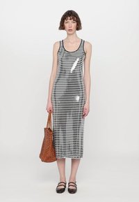Robe midi à rayures noires et blanches avec des sequins brillants, sans manches, col rond, accompagnée d'un sac tissé marron.