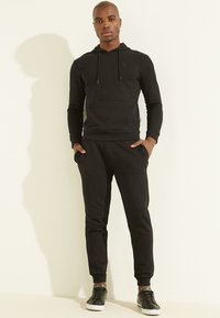 Zwarte hoodie met een kangoeroezak, trekkoorden en geribbelde manchetten, gecombineerd met bijpassende zwarte joggers en zwarte sneakers.