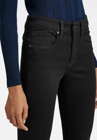 Svarta denimjeans med hög midja, sidofickor och kontrasterande sömmar. Materialet har en slät, något elastisk textur.