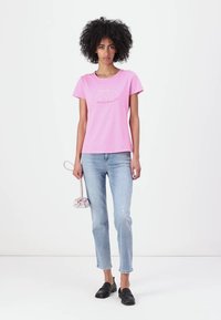 T-shirt di cotone rosa con scollatura rotonda, maniche corte e dettagli ricamati sul davanti; abbinata a jeans slim blu chiaro.