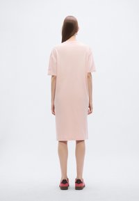 Ροζ φόρεμα από τζέρσεϊ μέχρι το γόνατο με κοντά μανίκια, άνετη γραμμή, στρογγυλή λαιμόκοψη και λεία υφή, συνδυασμένο με κόκκινες και μαύρες αθλητικές παπουτσιές.