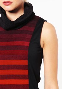 Oberteil mit Kapuze, das auffällige horizontale Streifen in Rot und Burgunderrot aufweist, kombiniert mit einem schwarzen Abschnitt; weiche Stofftextur.